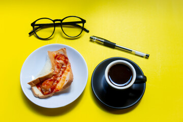 My snacks, ketchup sandwiches in a white plate and black coffee on a yellow desk.