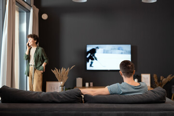 Back view of young man sitting in front of tv set and watching sports news