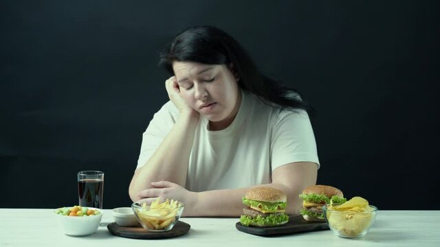 Young upset overweight woman tired of diets with junk food. Dieting restricts, compulsive overeating, unhealthy eating