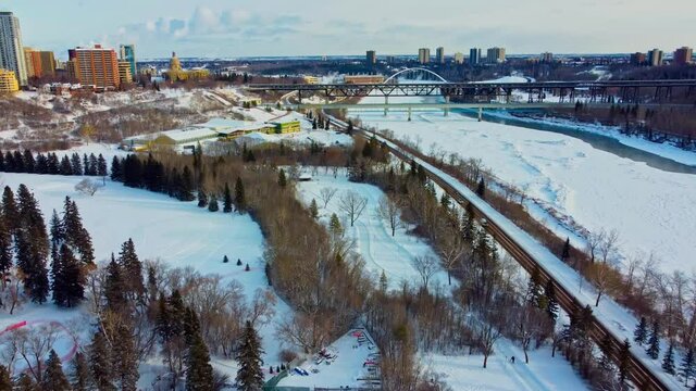 Aerial winter flyover drop at Victoria Park manmade quiet ice rink connected to an infinity skate track next to forest road snow covered North Saskatchewan river by Royal Glenora club downtown city3-4