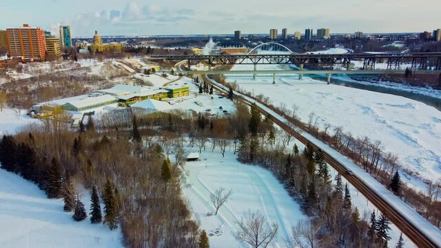 Aerial winter flyover drop at Victoria Park manmade quiet ice rink connected to an infinity skate track next to forest road snow covered North Saskatchewan river by Royal Glenora club downtown city4-4