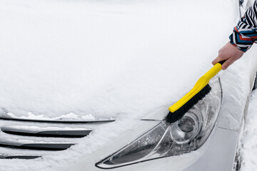 Man brushing snow and ice from headlight of car with brush. Person cleaning fresh snow from car in the winter