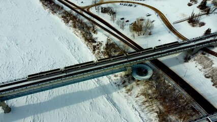Aerial winter dolly roll birds eye view from vintage historic high level bridge to the public transit train bridge of Dudley B Menzies while 5 accordian trains cross from downtown to uptown Whyte Ave