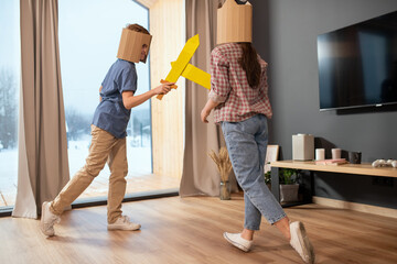 Playful siblings in casualwear and cardboard helmets fighting with toy swords