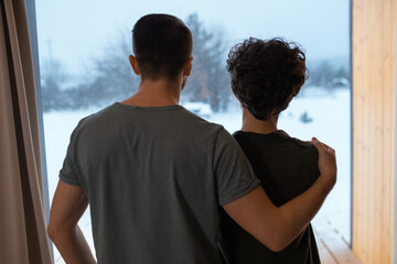 Rear view of young affectionate relaxed couple standing by large window