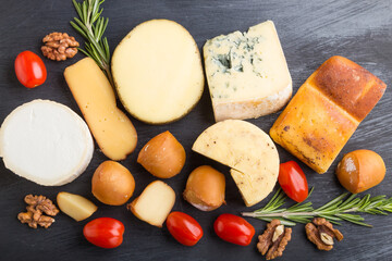 Set of different types of cheese with rosemary and tomatoes on a black wooden background . Top view.