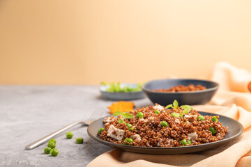 Quinoa porridge with green pea and chicken on ceramic plate on a gray concrete background. Side view, copy space.
