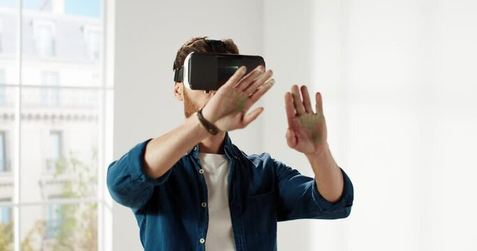 Close up of Caucasian bearded man in virtual reality helmet standing in new apartment and using gestures browsing catalog. Slow motion.