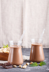 Organic non dairy pistache chocolate milk in glass and wooden plate with pistache nuts on a gray concrete background.