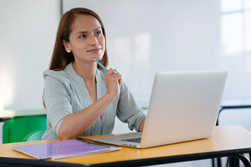 Teacher in the classroom sitting in front of the computer thinking and looking pensive