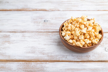 Popcorn with caramel in wooden bowl on a white wooden background. Side view, copy space.