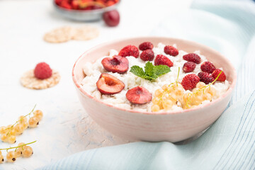 Rice flakes porridge with milk and strawberry in ceramic bowl on white concrete background. Side view, selective focus.