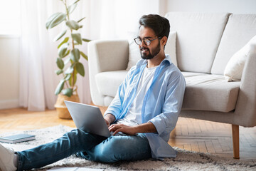 Home Office. Handsome Eastern Male Freelancer Working With Laptop In Living Room