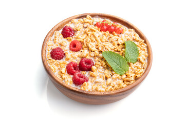 Wheat flakes porridge with milk, raspberry and currant in wooden bowl on white background. Side view, close up.