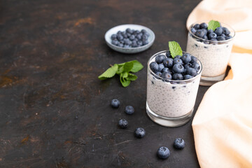 Fototapeta na wymiar Yogurt with blueberry and chia in glass on black concrete background. Side view, copy space.