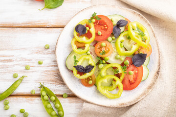 Vegetarian salad from green pea, tomatoes, pepper and basil on white wooden background. top view, close up, selective focus.