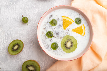 Fototapeta na wymiar Yogurt with kiwi, gooseberry, chia in ceramic bowl on gray concrete background. top view, flat lay, close up.