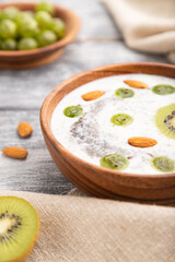 Yogurt with kiwi, gooseberry, chia and almonds in wooden bowl on gray wooden background. Side view, close up, selective focus.