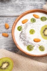 Yogurt with kiwi, gooseberry, chia and almonds in wooden bowl on gray wooden background. Side view, close up,selective focus.