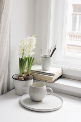 Easter spring still life. Cup of coffee, book and blank diary near window sill. White hyacinth in flower pot. Pencils in ceramic holder. Home office concept. Scandinavian interior. Vertical.