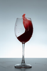 Splash of red wine in a glass on a gray background.