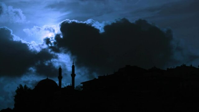 Dark clouds in front of the full moon with the building silhouettes in a dark blue night