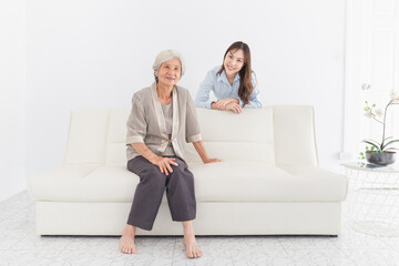 Obraz premium young Asian female hug old female in home, they feeling happy and smile, they sitting on sofa, mother's day, happiness elderly in family time