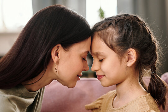 Side view of young brunette woman and her little daughter touching by foreheads