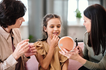 Little girl in dress applying nutritious balm on lips while looking in mirror