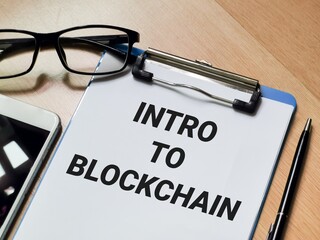 Business and technology concept. Phrase INTRO TO BLOCKCHAIN written on paper clipboard with pen,smartphone and eye glasses. 