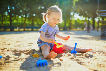 Adorable little girl having fun on playground in sandpit