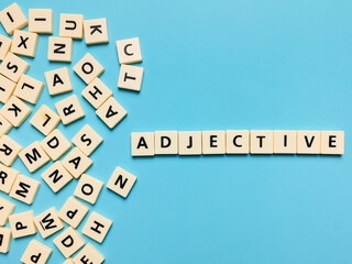 ADJECTIVE word made from square letter tiles on blue background.