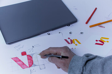 Graphic designer designs a logo against a background of sketches and drawings on a table. Printed...