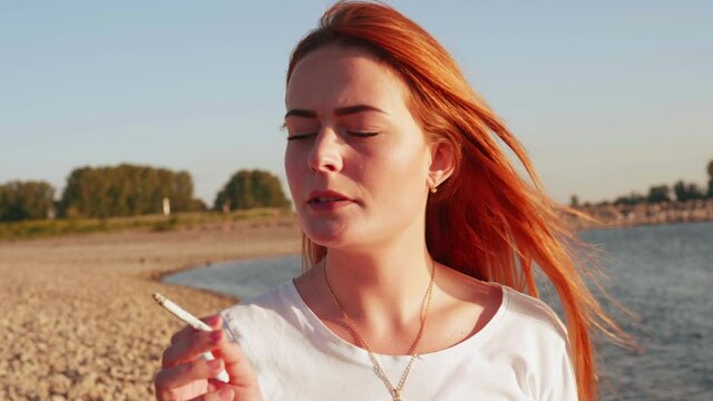 [4k] young attractive woman smoking a cigarette at the beach in sunset