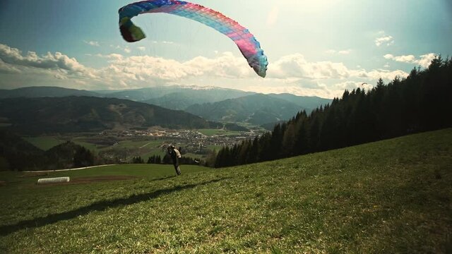 Paraglider takes off from a hill. It runs up, raises its wing, and lifts off from the ground.