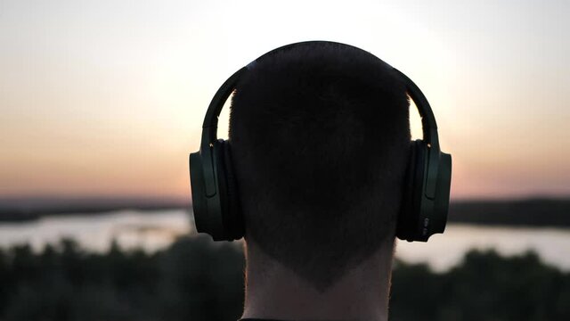 Silhouette Of A Young Man Wearing Headphones On His Head Against The Backdrop Of Sunset. Slow Motion Video.