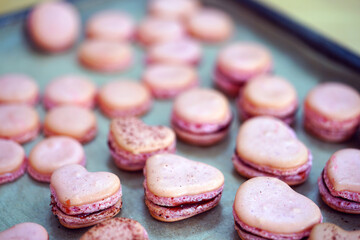 Pink heart homemade macaron cookies filled with raspberry jam on parchment paper on a baking sheet