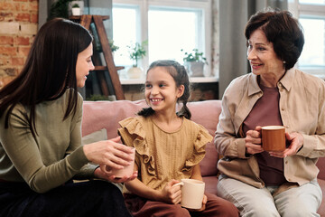 Two contemporary females in casualwear and adorable little girl with hot drinks
