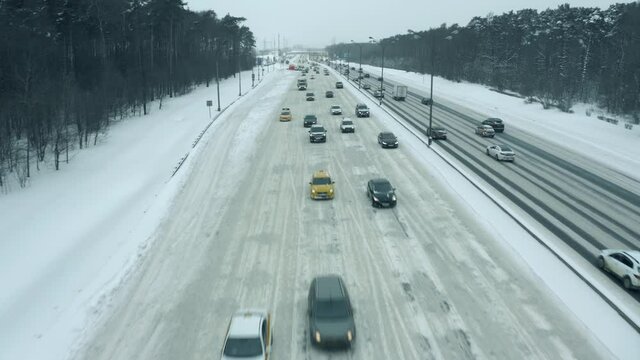 Low altitude aerial view of cars driving along the snow covered highway in winter