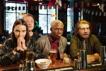 Group of young intercultural friends watching football broadcast together in pub