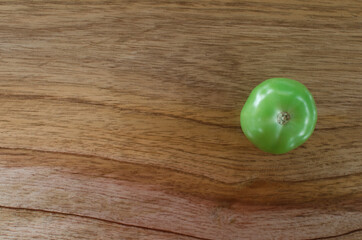 Fotografía de jitomate verde sobre una tabla con texturas de madera rústica