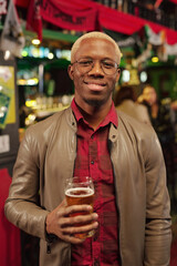 Young cheerful African man looking at you with smile while toasting with beer
