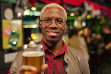 Happy young African man in eyeglasses and casualwear toasting with beer