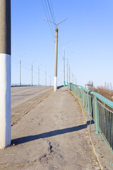 concrete road and pillars going into the distance, and on the right is a green fence