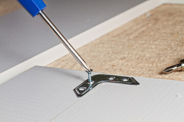 Obraz premium The screwdriver twists the screw into a brown wooden board in the corner, horizontal photo