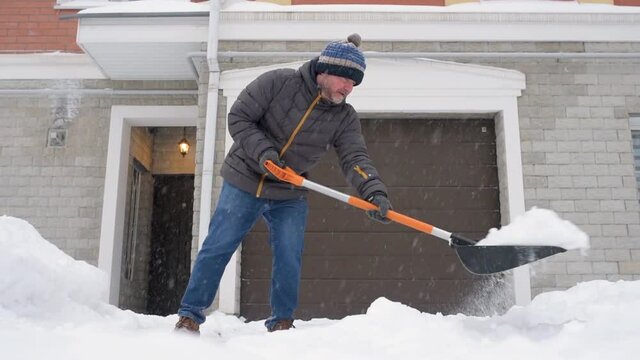 A mature man clean path near house from snow during strong blizzard. Person shoveling snow out of the driveway. Huge snowdrifts. Difficult situation in the city after a snow storm