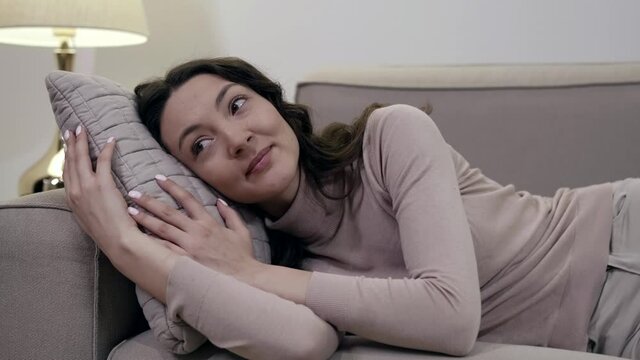 A happy smiling woman lying on a sofa, on a pillow, enjoying a rest in a bright room.