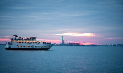 Ferry boat to the left of the statue of liberty during sunset