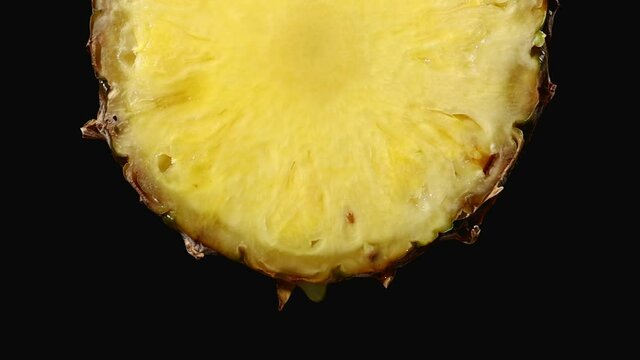 freshly squeezed pineapple juice drops from the ripe yellow fruit slice close - up on a black background slow motion