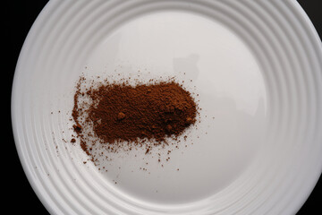 Cocoa powder on a white plate on a black background. Top view.